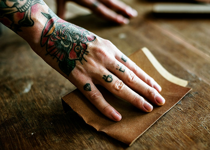 Close-up of tattooed hands sanding a wooden surface, symbolizing the mystery and personal experience of disappearance cases.