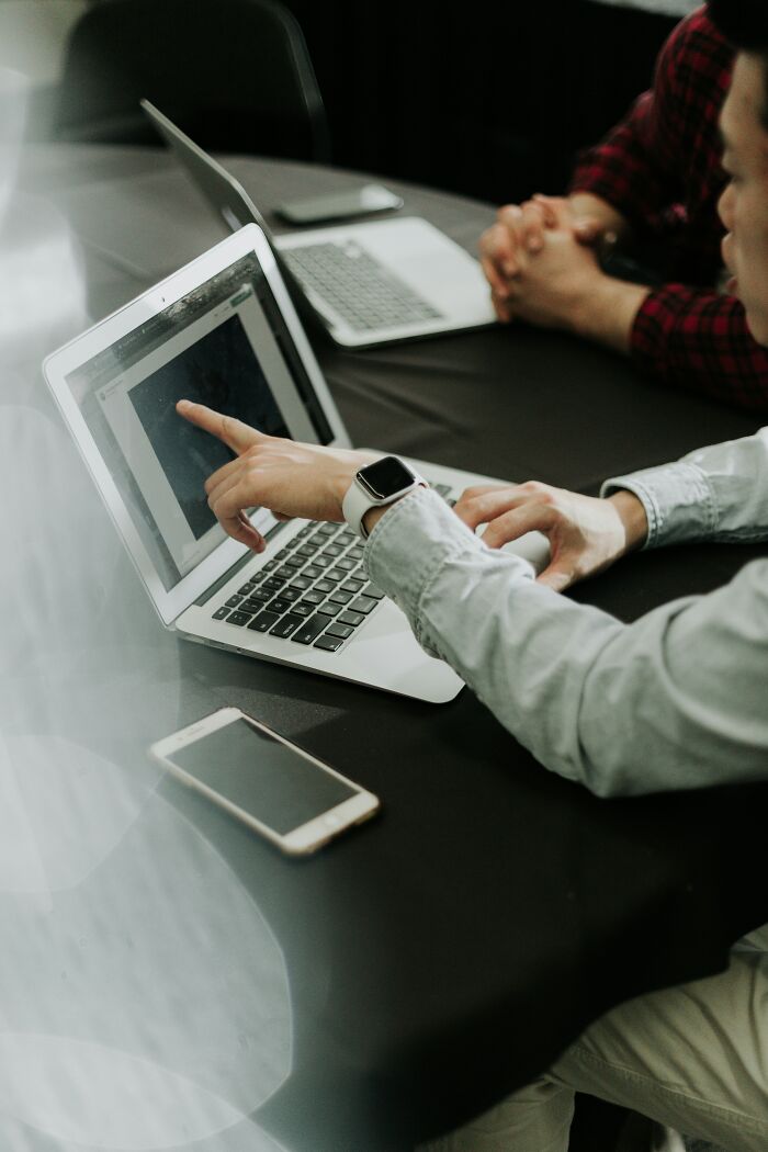 Two people discussing industry secrets on a laptop during a business meeting at a black table with a smartphone nearby - 21