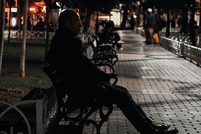 Man sitting alone on a park bench at night, evoking creepy experiences and unsettling quiet moments in the dark.