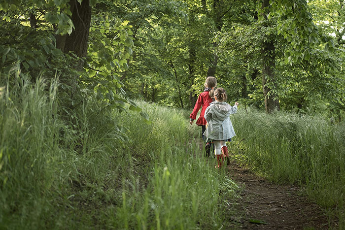 Two children walking along a forest path surrounded by tall grass and green trees, evoking creepy experiences atmosphere.