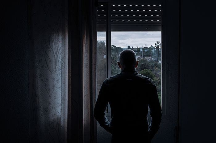 Man standing in a dark room looking out the window, reflecting on creepy experiences from time to time.