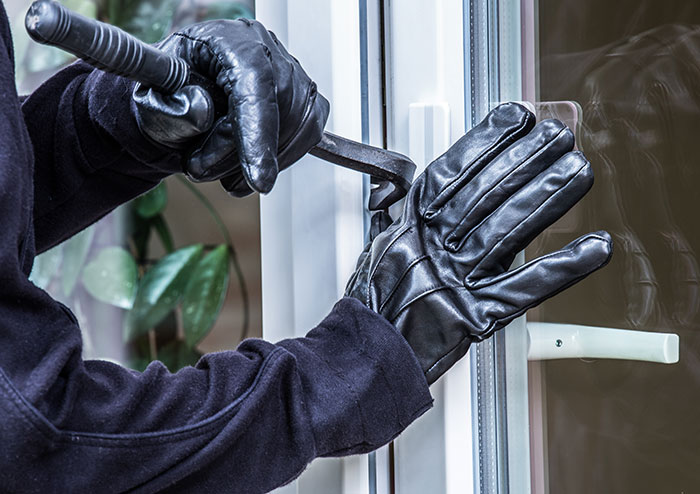 Person wearing black gloves using crowbar to break into a glass door illustrating creepy experiences people still think about.
