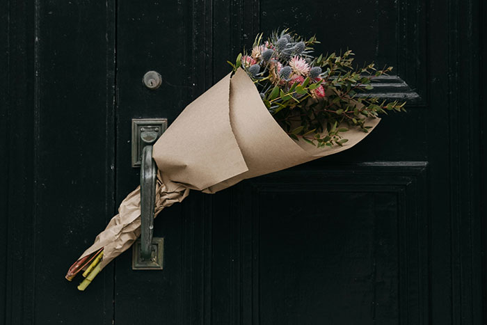 Bouquet of flowers wrapped in brown paper stuck in a black door handle, evoking creepy experiences and eerie feelings.