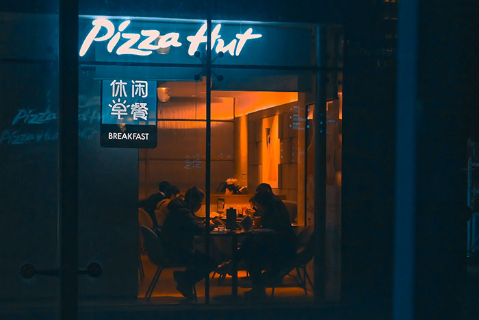 People sitting inside a dimly lit Pizza Hut at night, evoking a creepy experience atmosphere.