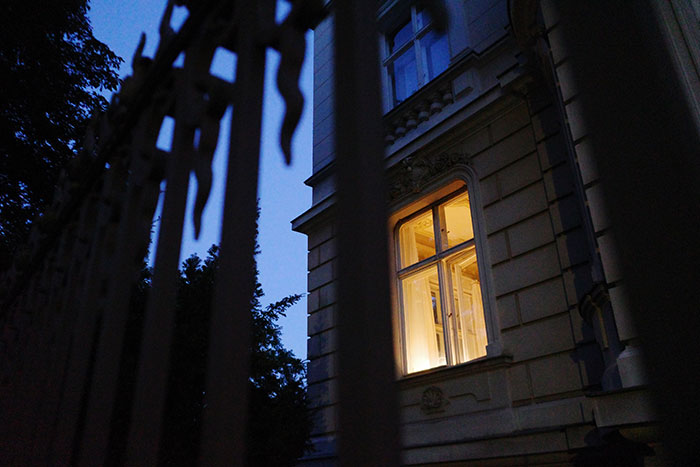 Dimly lit window of an old building seen through a wrought iron fence, evoking creepy experiences at night.