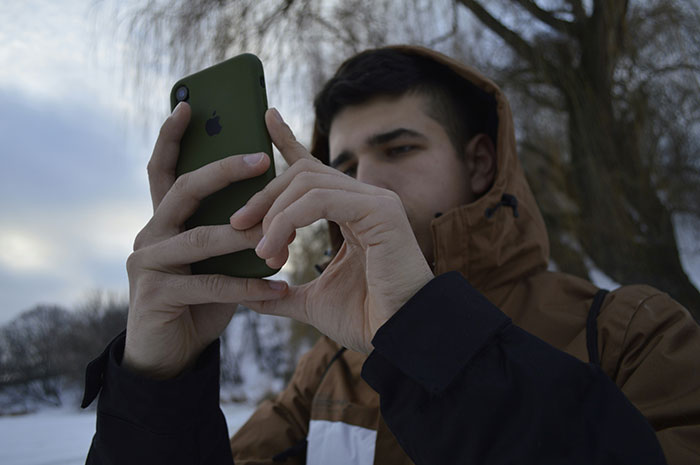 Young man in a brown jacket using a smartphone outdoors, reflecting on creepy experiences in a cold, snowy setting.