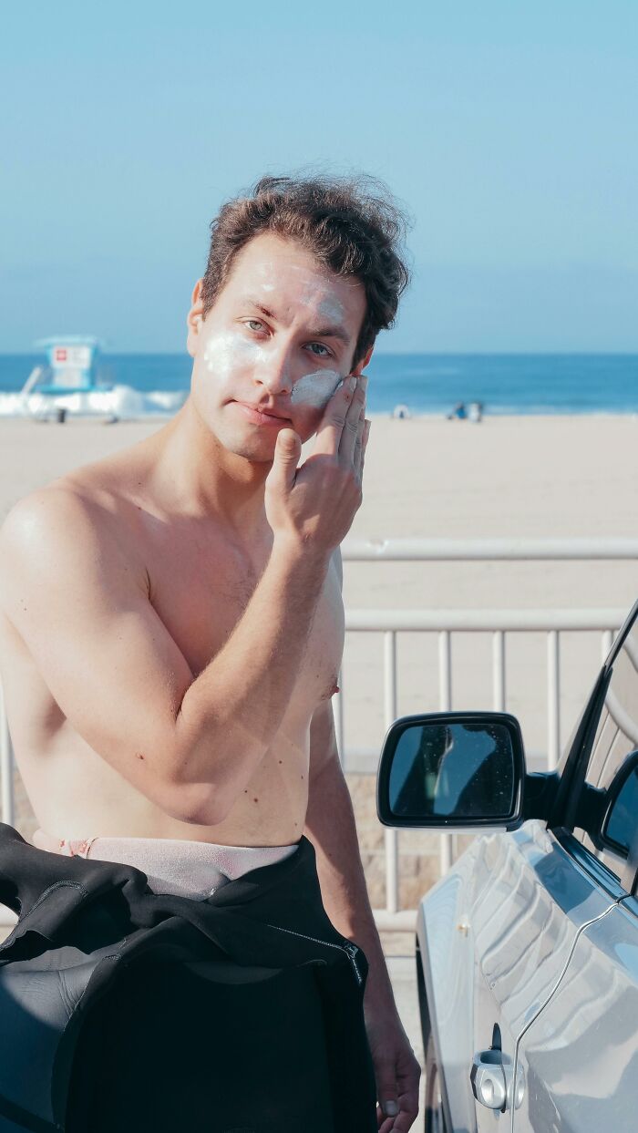 Shirtless man at the beach applying sunscreen, illustrating things people thought were a flex but aren’t.