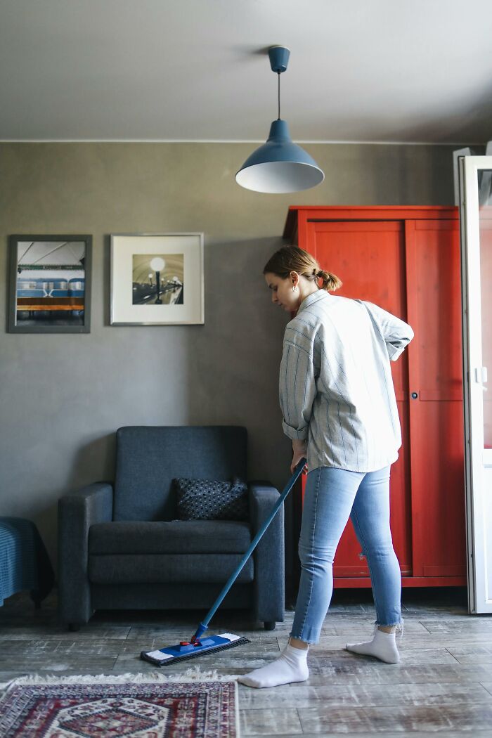 Woman cleaning floor with mop in living room showing things people thought were a flex but actually aren’t concept.