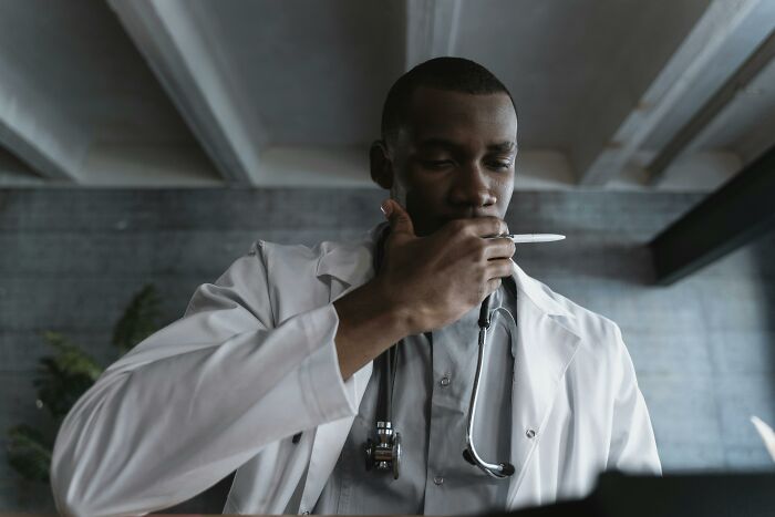 Male doctor in white coat holding a pen to his mouth, reflecting on disturbing facts he wishes he didn’t know