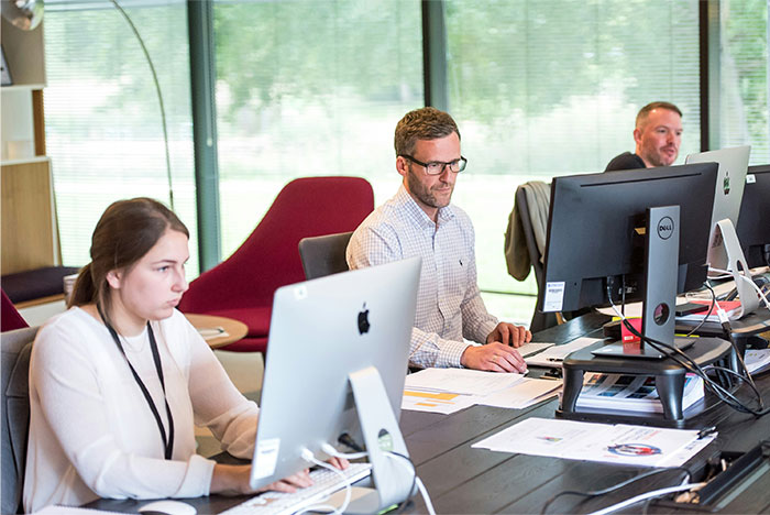 Three office workers focused on computer screens in a modern workspace, depicting the reality of working at a dying company.