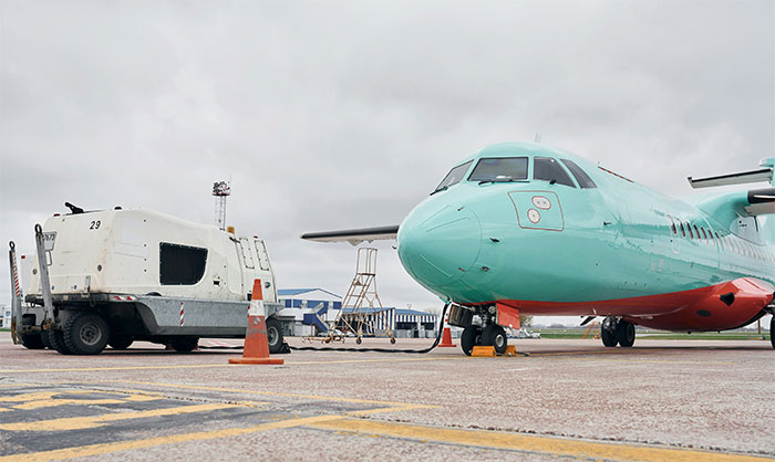 Small teal airplane grounded on runway near airport equipment under cloudy sky, symbolizing overworked and underpaid conditions.