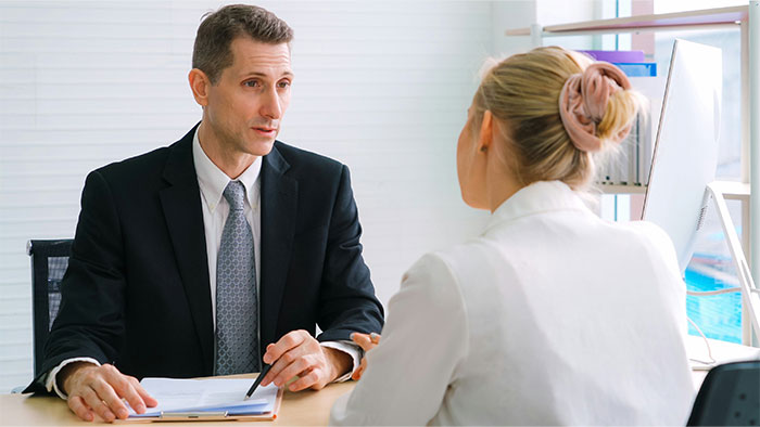 Man in a suit discussing work concerns with a woman in an office, illustrating challenges of overworked and underpaid employees.