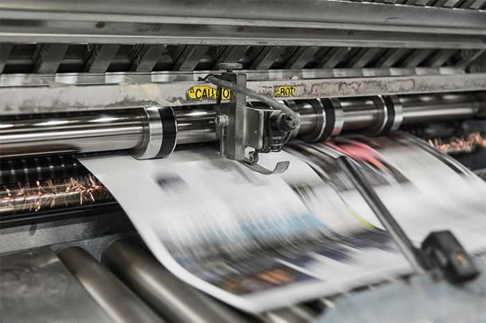 Printing press producing fast-moving newspapers, symbolizing overworked and underpaid employees at a dying company.