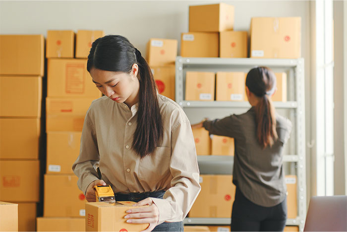 Two women packing boxes in a warehouse, illustrating the experience of working at an overworked and underpaid company.