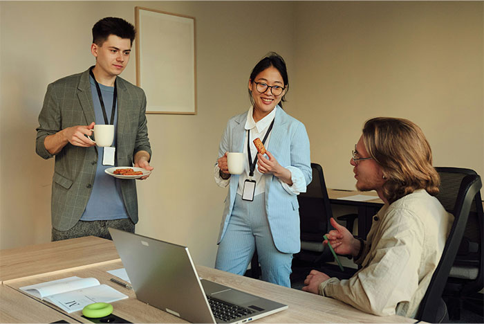 Three coworkers taking a break with coffee and snacks, discussing work at an overworked and underpaid dying company.