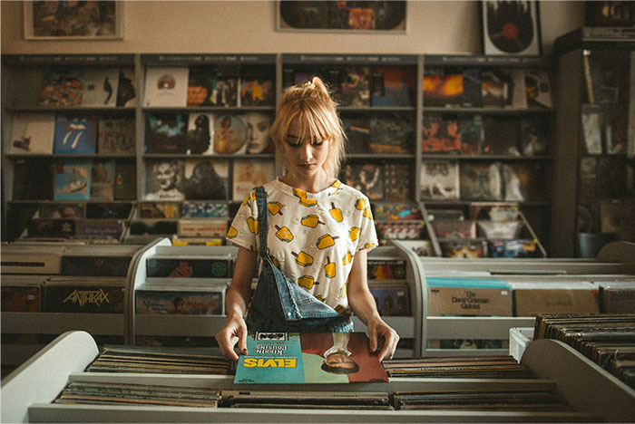 Young woman browsing vinyl records in a store, reflecting the mood of being overworked and underpaid at a dying company.