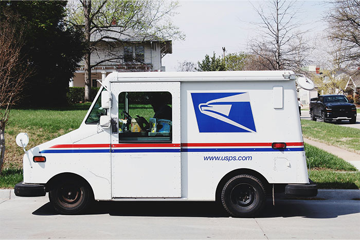 USPS mail delivery truck parked on a suburban street representing overworked and underpaid workers in a dying company.