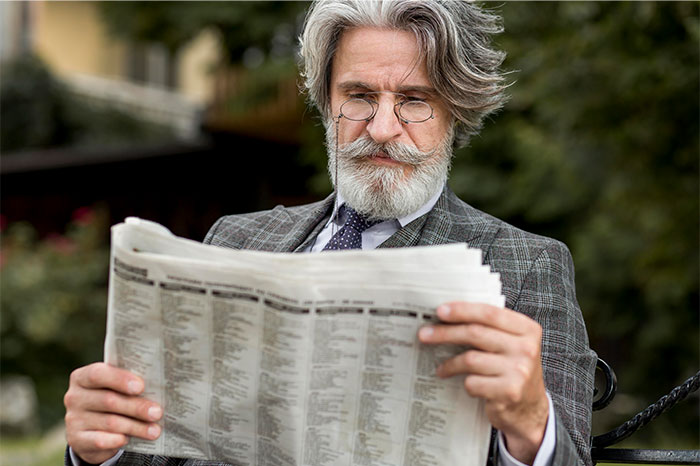 Older man with glasses reading a newspaper outdoors, reflecting on the realities of working at a dying company.