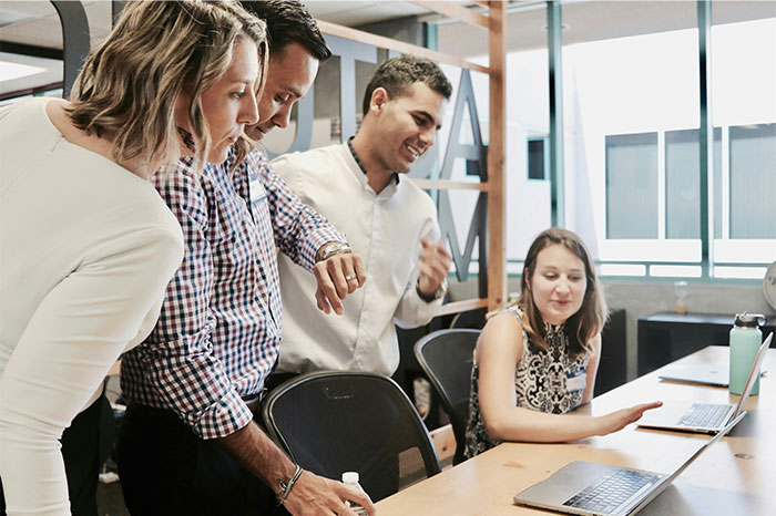 Four colleagues collaborating at a desk with laptops, illustrating challenges of working at a dying company.