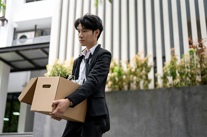 Young professional carrying a box of personal items, symbolizing overworked and underpaid employees leaving a dying company.