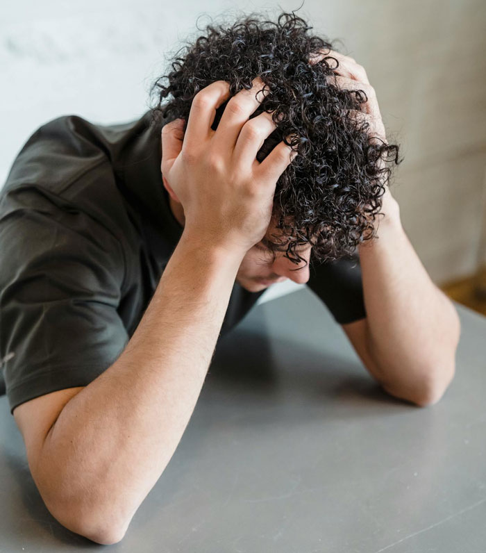 Nonbinary person frustrated, holding head in hands while dealing with roommates’ boyfriends using private bathroom conflict. Nonbinary person frustrated, holding head in hands while dealing with roommates’ boyfriends using private bathroom conflict.