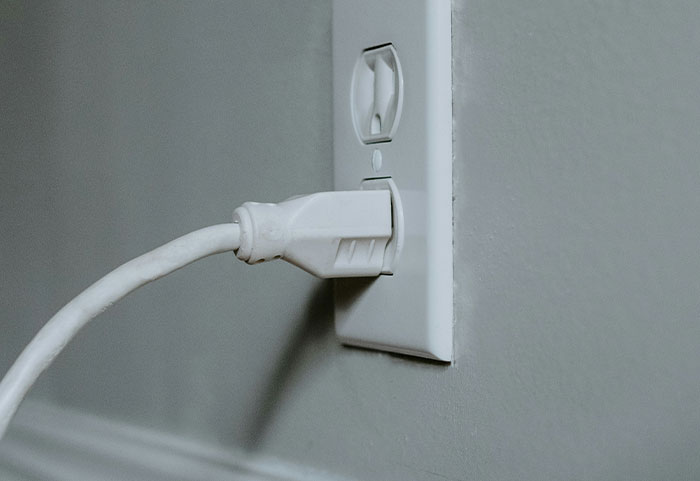 Close-up of a white electrical plug partially inserted into a wall outlet, illustrating petty neighbor power disputes.