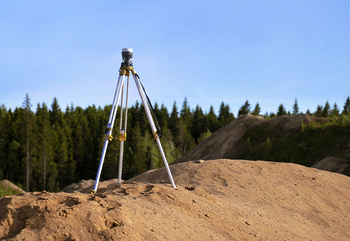 Tripod surveying equipment set on dirt mound near forest, illustrating petty neighbor boundary disputes posted online.