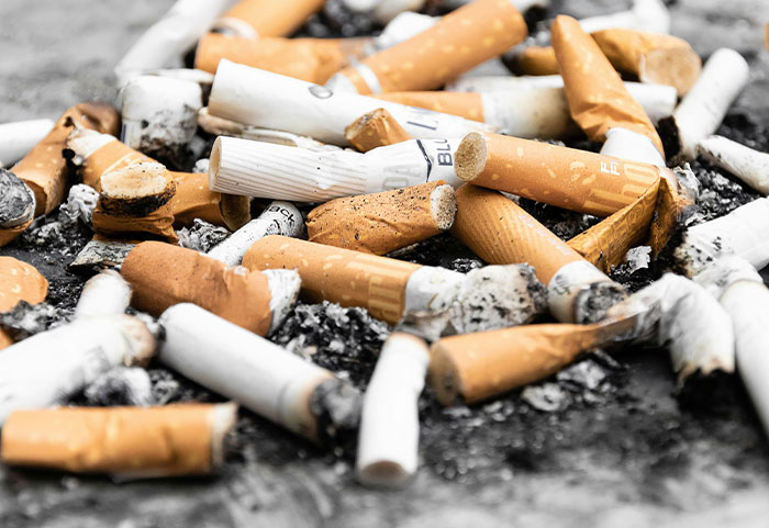 Pile of cigarette butts and ashes symbolizing petty neighbors being shamed online for littering and bad behavior.