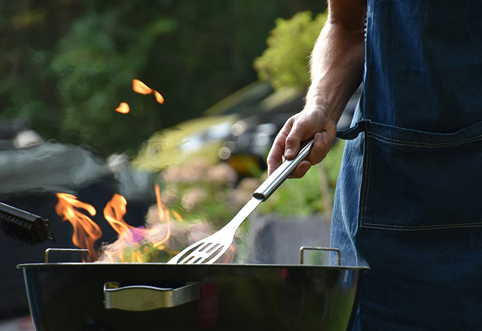Person grilling outdoors with visible flames, illustrating petty neighbor conflicts shared online in a suburban setting.