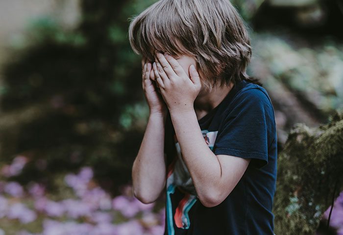 Child covering face outdoors expressing emotion, representing petty neighbors shamed online in a community setting.