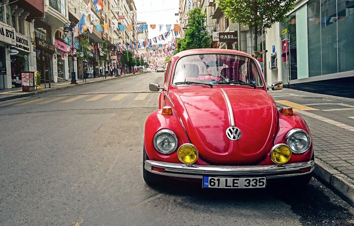 Vintage red Volkswagen Beetle parked on a city street, representing unexpected wedding registry items like a coffin.