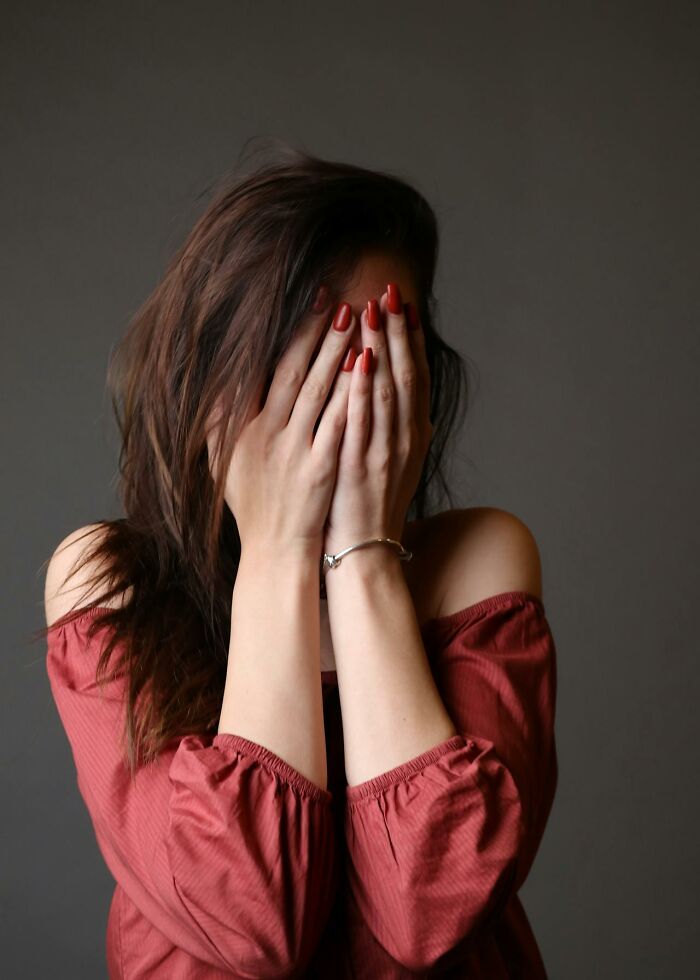 Woman covering her face with hands wearing a red top, illustrating people actually experiencing psychic predictions.