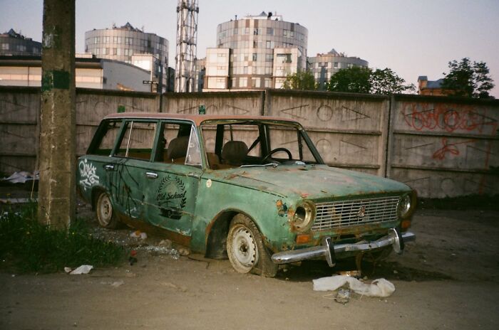 Old rusty green car abandoned beside a concrete wall, showing heartwarming and harmless secrets of decay over time.