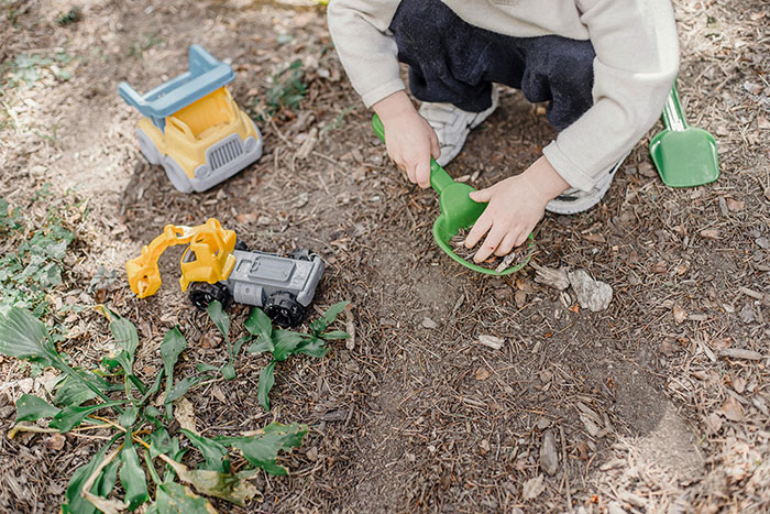 Toddler playing in dirt with toy trucks and gardening tools, illustrating the no such thing as a clean toddler concept.
