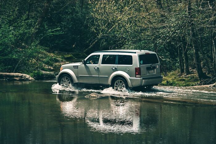 Silver SUV driving through a shallow forest river, reflecting in the water, representing experiences people had with psychic predictions
