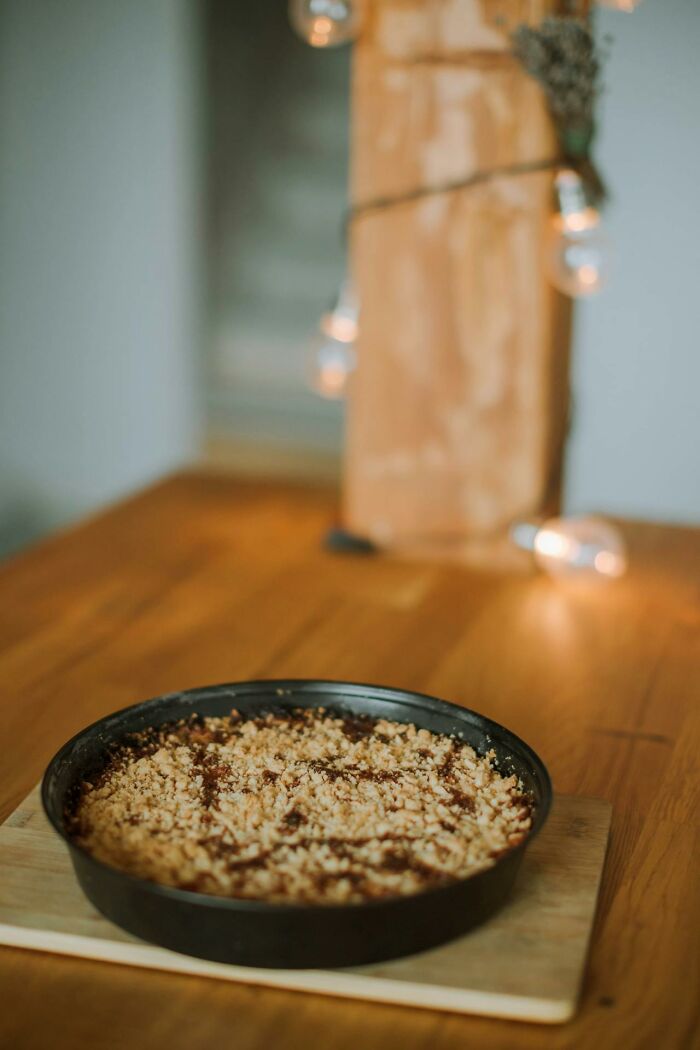 Crumb-topped dessert in a black pan on a wooden table, softly lit with warm decorative lights in the background.