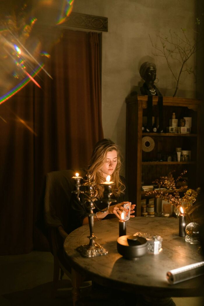 Woman holding tarot cards by candlelight in a dim room, illustrating psychic predictions being experienced.