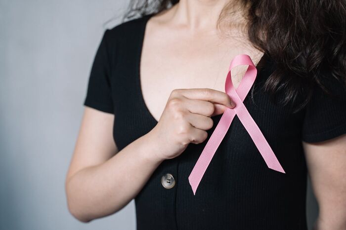 Person wearing a black shirt holding a pink ribbon symbolizing hope and good news in health awareness campaigns.