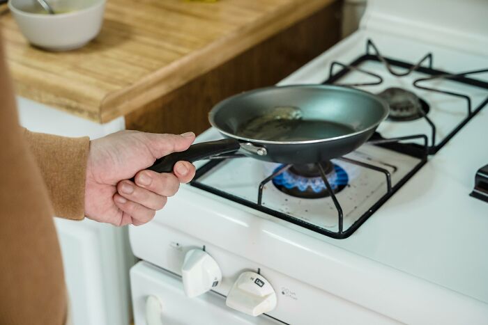 Person holding a frying pan over a gas stove burner illustrating tiny human mistakes that changed history.