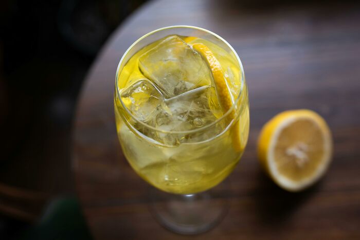 Glass of iced lemon drink with ice cubes and lemon slice on wooden table, symbolizing tiny human mistakes.