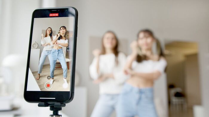 Two women recording a dance video on a smartphone, illustrating popular unsolved mysteries of viral trends.