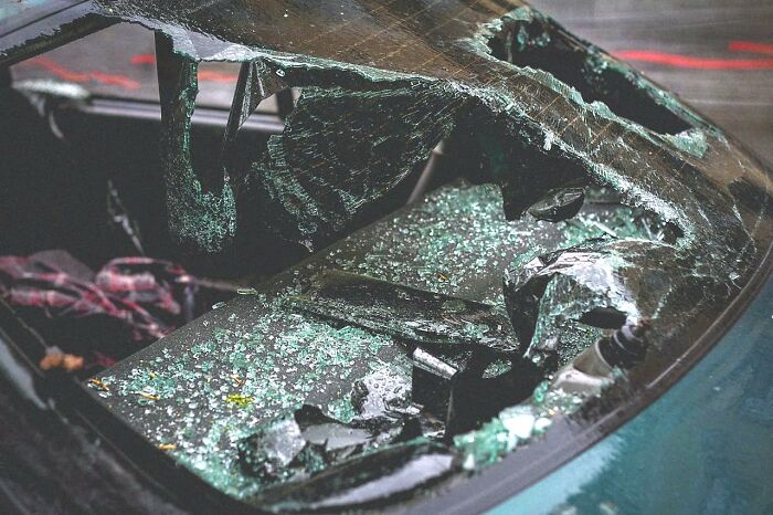 Shattered car window with broken glass scattered inside, illustrating creepy and disturbing scenes police officers encountered at homes.