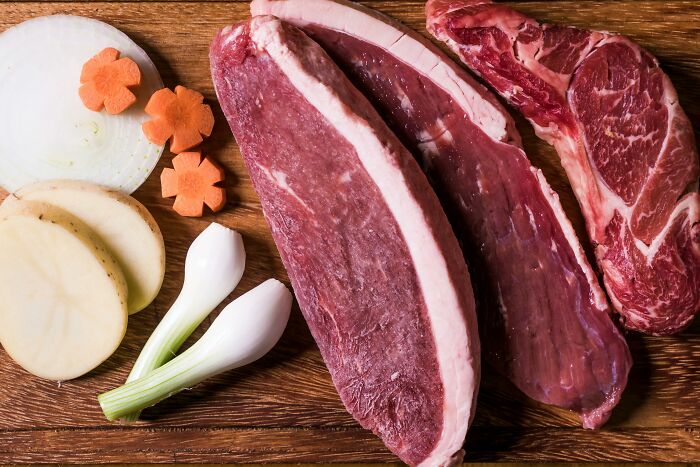 Raw beef cuts with sliced vegetables on a wooden board, illustrating creative ways to avoid babysitting online.