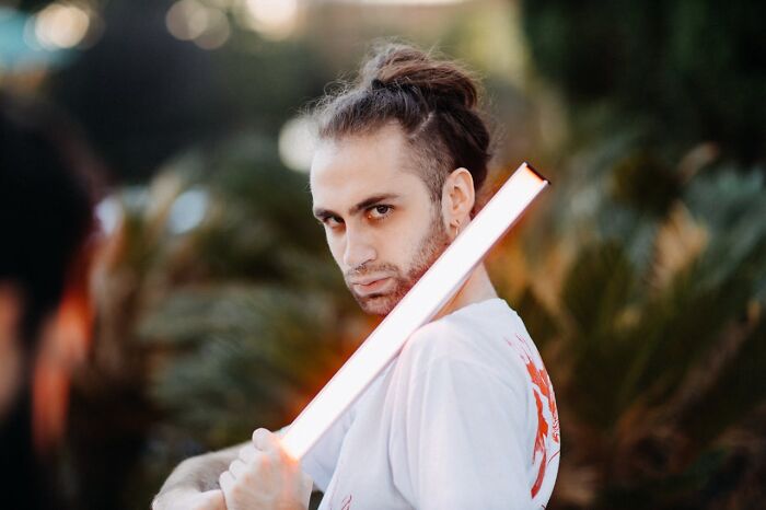 Person with a man bun holding a glowing light stick outdoors, illustrating the unexpected items on wedding registries including a coffin.