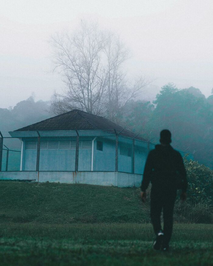 Silhouetted night shift worker walking toward a fenced building in foggy, eerie surroundings suggesting paranormal encounters.