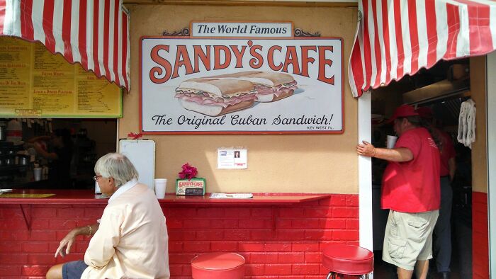 Outdoor view of Sandy's Cafe with red stools and striped awning, illustrating tiny human mistakes that changed history.