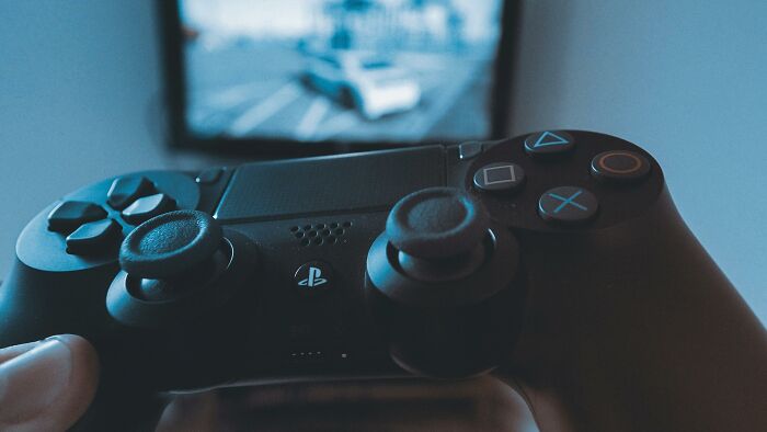 Close-up of a person holding a PlayStation controller while playing a racing video game on a screen.