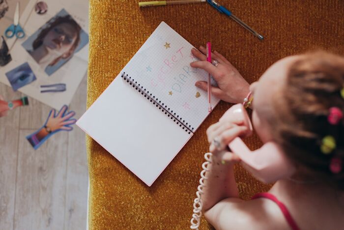 Teen girl with colorful hair clips, writing in a secret diary while talking on a pink phone, revealing hidden side of teens. - 6