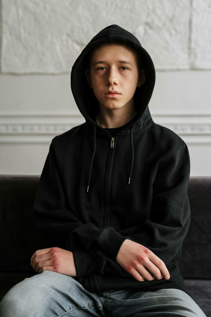 Teenager wearing black hoodie sitting solemnly indoors, representing resilience in people surviving crazy situations.