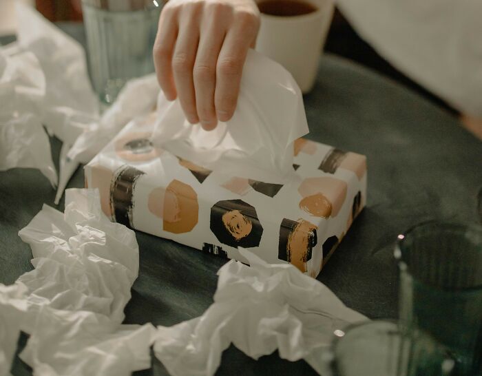 Hand pulling tissue from a box surrounded by used tissues, illustrating gross and unexpected things witnessed in strangers’ homes.